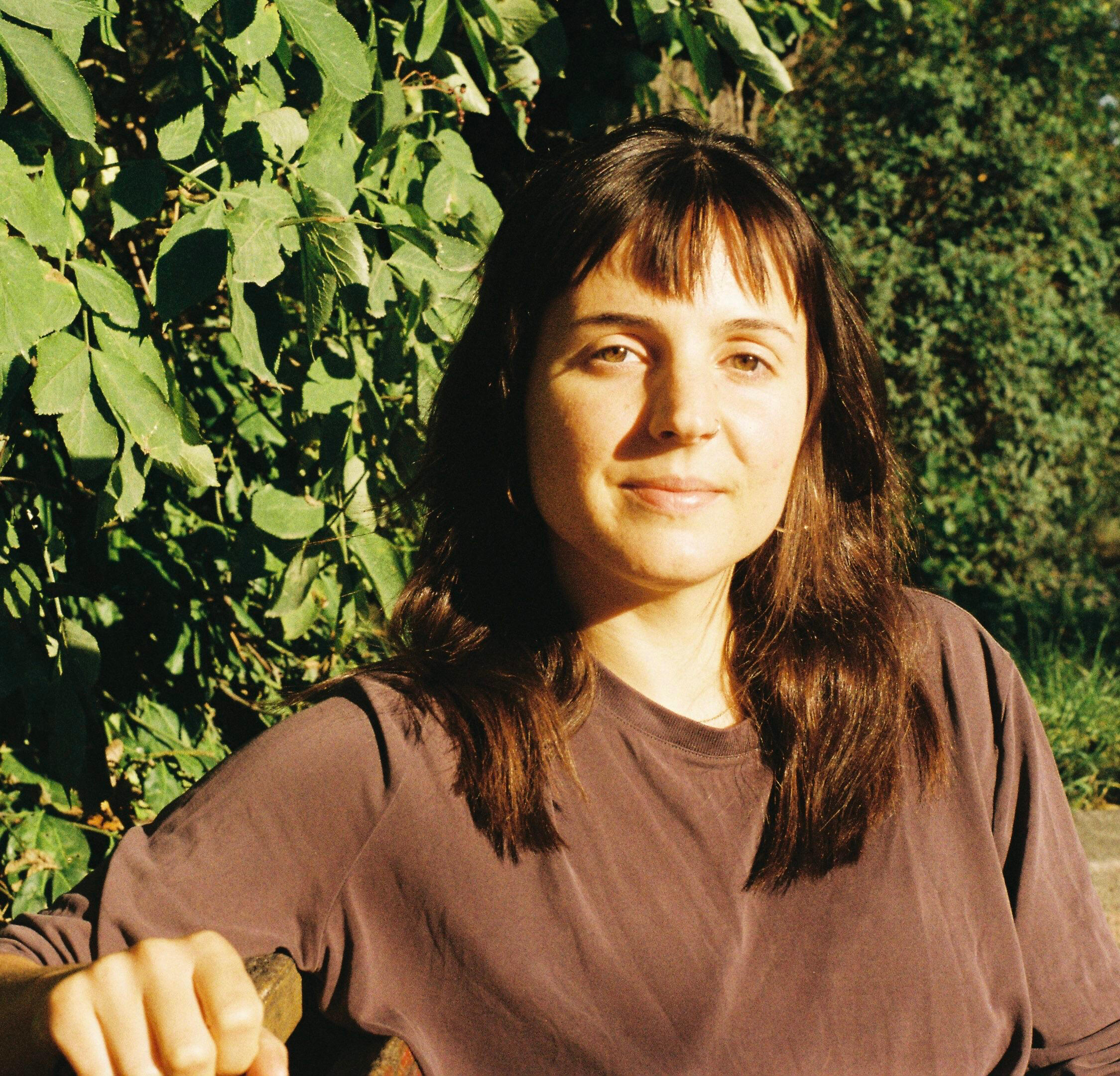 Porträt von Tifenn Corre, Hebamme aus Berlin, vor grünem Laub im Sonnenlicht